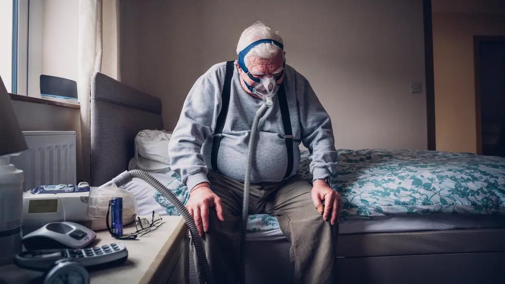 older man on cpap machine sitting on bed