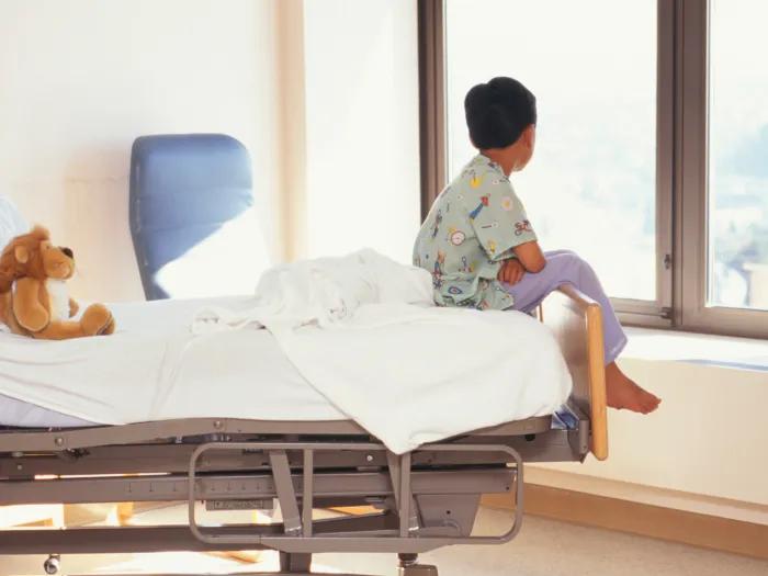 patient end of bed in hospital looking out window with stuffed animal on bed