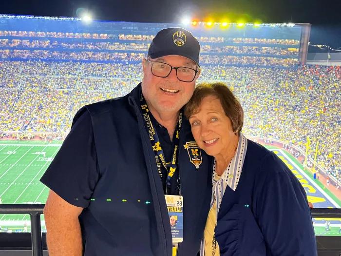 man and woman in front of stadium with crowd at UM