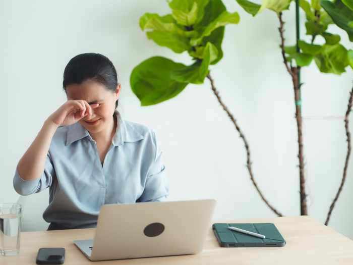 woman sitting by laptop putting hands on eyes