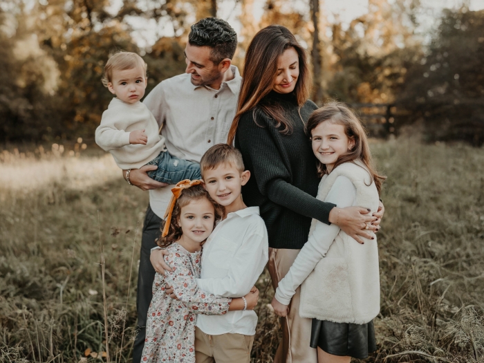 family photo mom dad and four kids in soft white beige and black clothes outside in field with trees behind