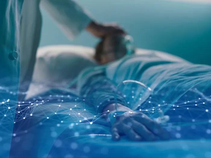 A clinician tends to a patient in a hospital bed. The image is overlaid with a graphical rendering of data.