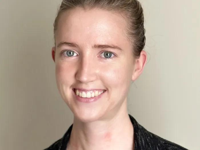 Young woman with dark blond hair swept up in a bun, wearing a black jacket and V-neck blouse