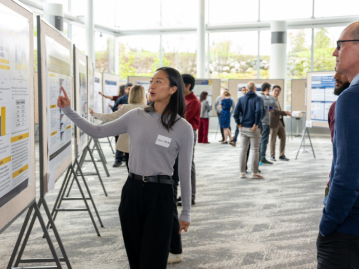 Attendees discuss research posters during the Department of Anesthesiology Research Retreat in a bright atrium at the North Campus Research Complex.