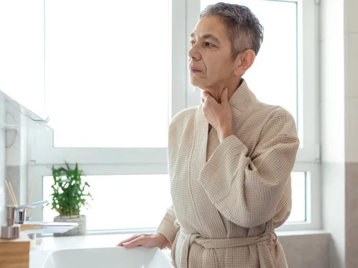 woman touching her neck in robe at home