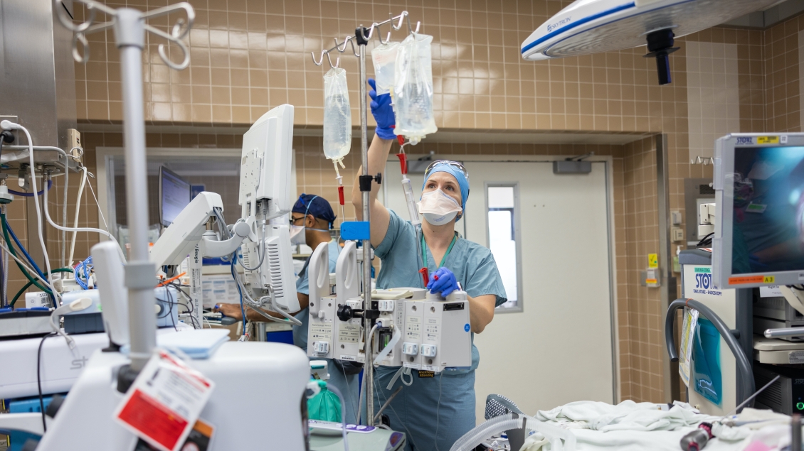 OR nurse reaches up to double check the IV bags for the patient surgery 