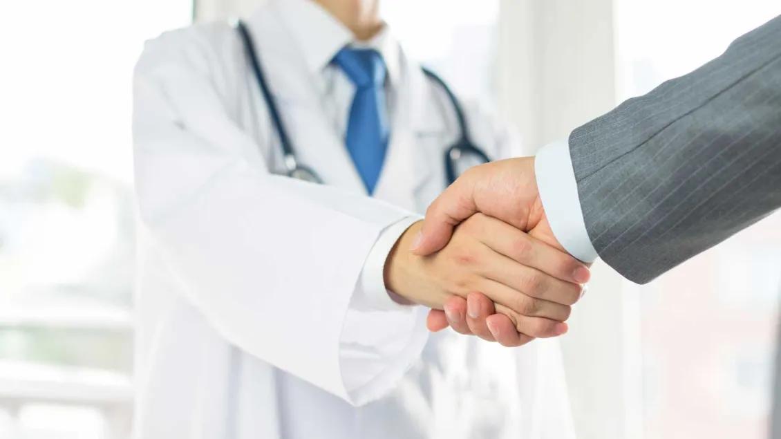 Medical professional in white coat shaking hands with man in suit