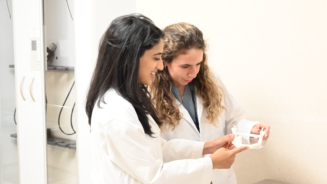 Two people in white lab coats looking at a 3D printed device