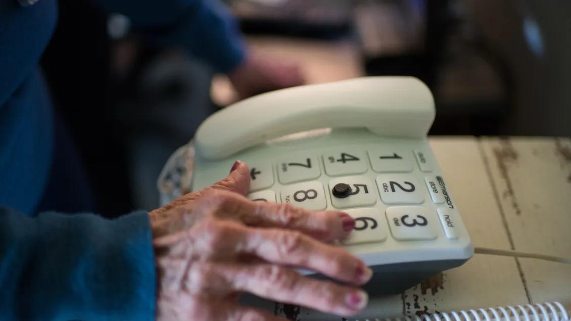 An elderly hand reaches for a large-button telephone.