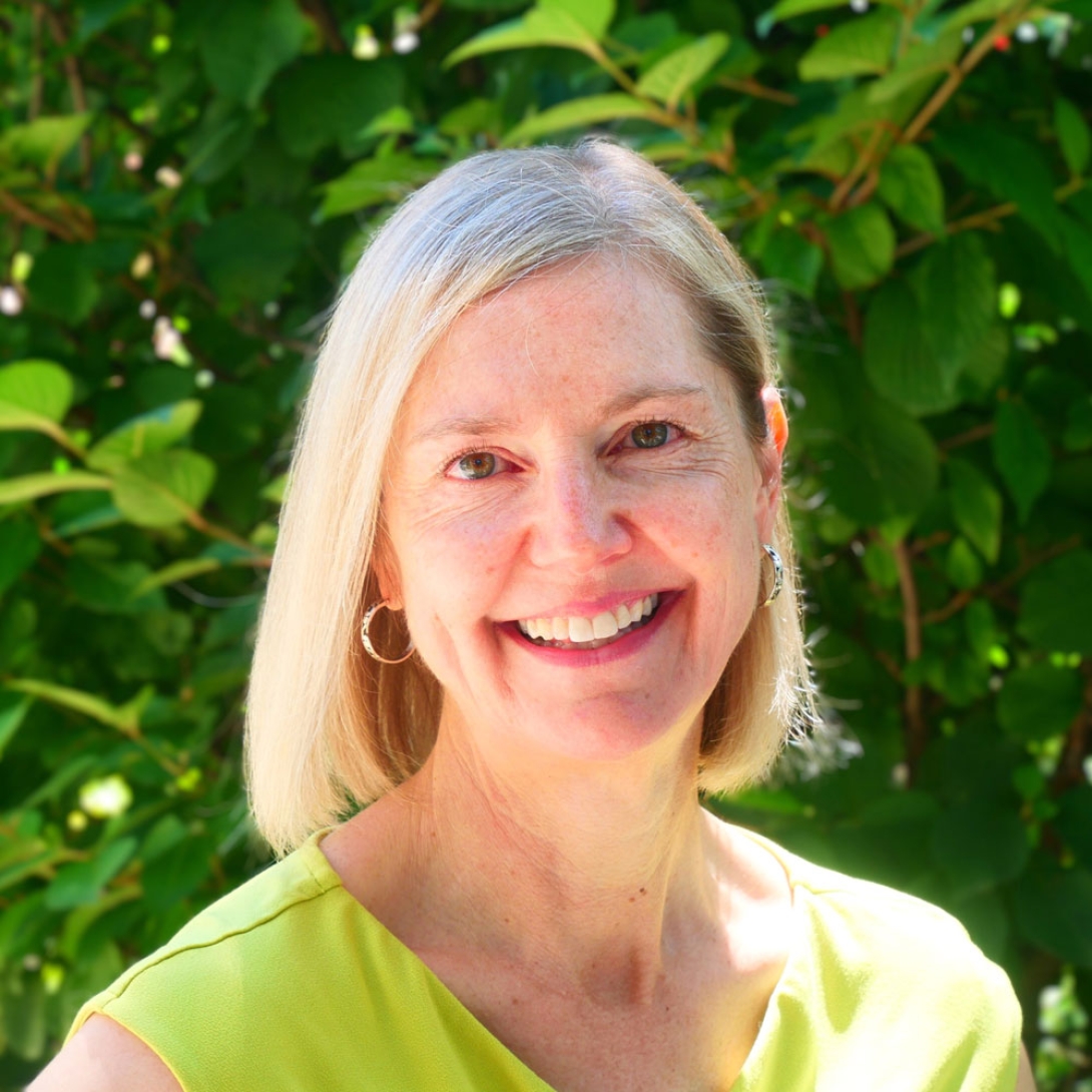 Susan Murphy smiling in front of green leaves