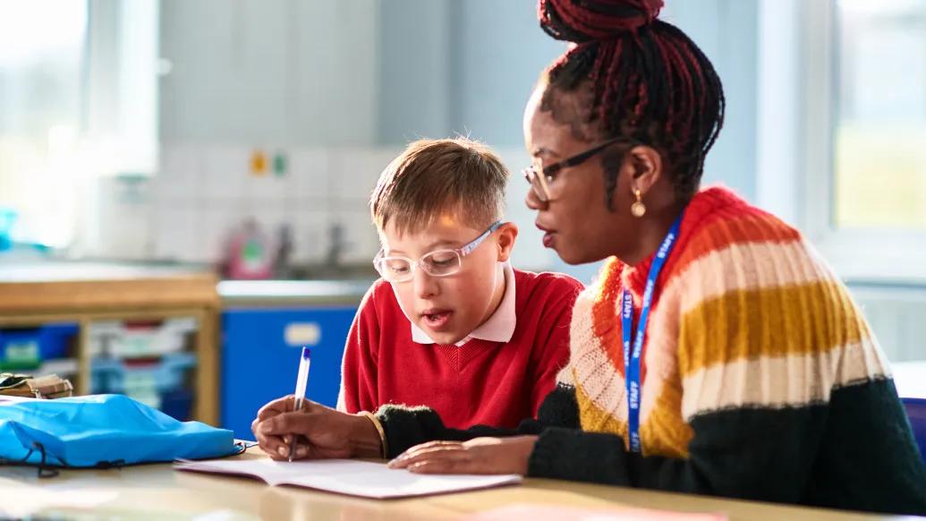 kid sitting with woman doing work at desk in classroom