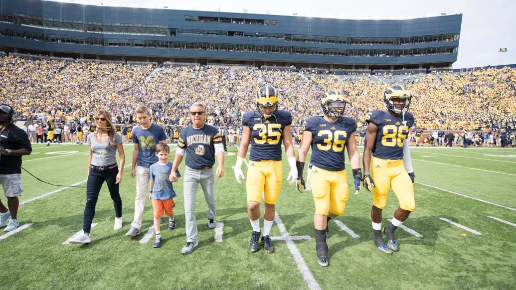 Nathan and Catherine Forbes were honorary captains during a 2015 Michigan Football game and are pictured on the field at Michigan Stadium with several players.