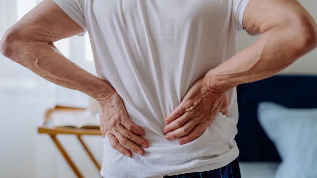 Main in a white t-shirt holding his lower back in pain