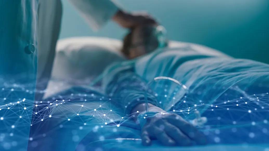 A clinician tends to a patient in a hospital bed. The image is overlaid with a graphical rendering of data.