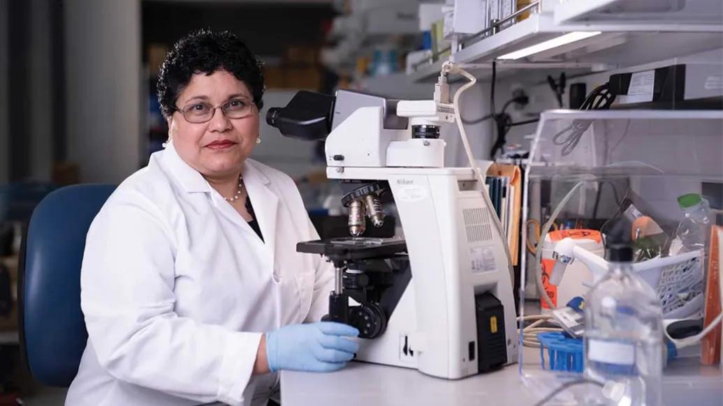Nisha D'Silva, BDS, MSD, PhD sits next to a microscope