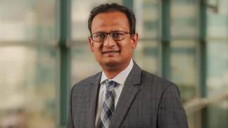 Dr. Nitin Jain standing in a hallway wearing a gray suit jacket and gray plaid tie