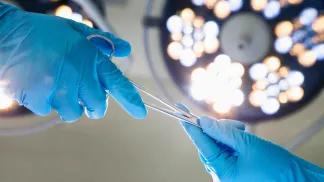 Person handing a surgical tool to another person under surgical lights