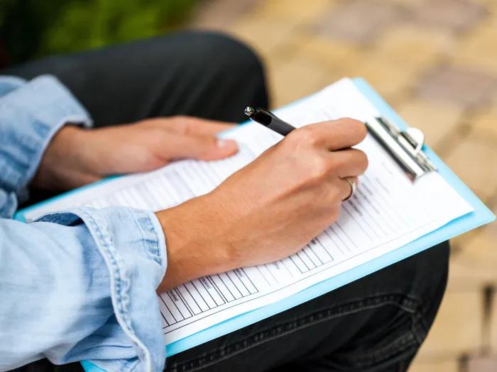 close-up of hands filling out form on clipboard