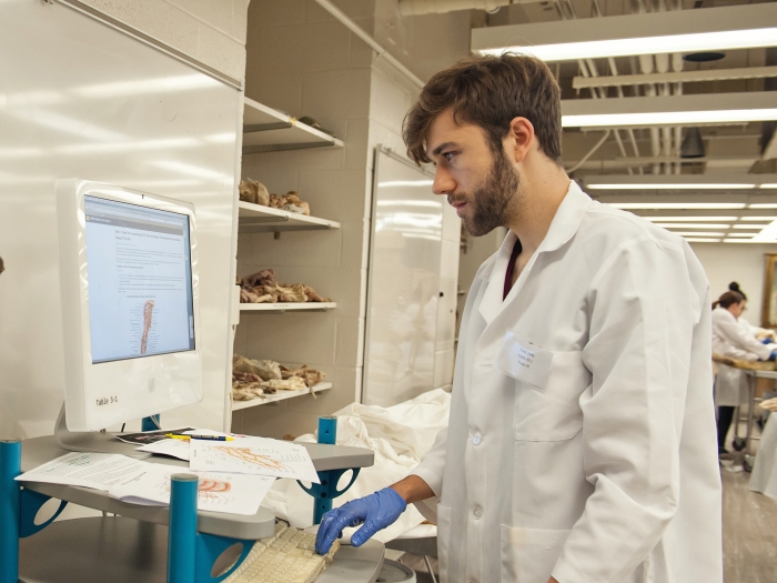 student stands at a computer next to a skeleton 