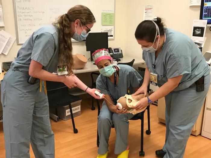 nurses gather round to practice holding techniques for a baby 
