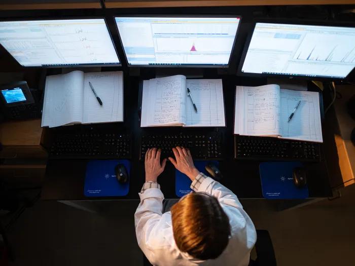 Photo taken from above of a female researcher in front of three monitors in the Metabolomics Core