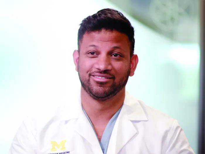 Video still of Shantanu Warhadpande wearing a white coat with a block M. 