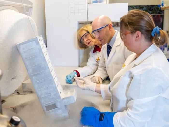 Three scientists in white lab coats examine a frosty container