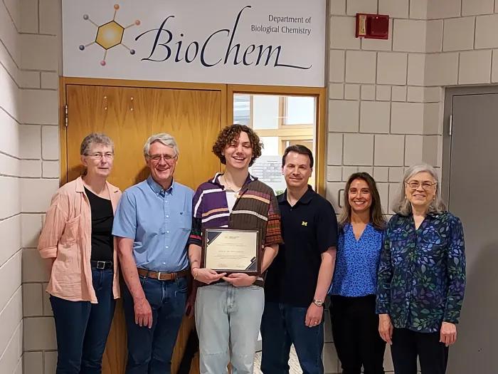 Ash de Borchgrave holding award certificate and flanked by advisors