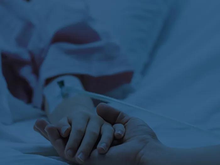 A person in a hospital bed holds hands with a visitor