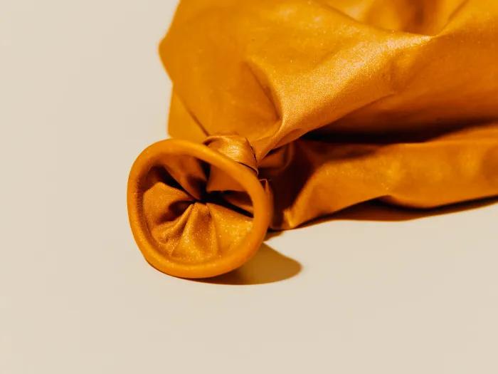 deflated orange balloon on white background close up on the part that's blown into