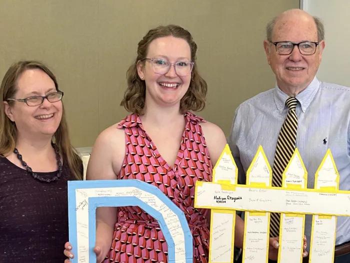 Madison Fitzgerald, Ph.D., after her defense, holding the department's D# sign. Every M&I grad student signs it after defending. Left to right: Melanie Pearson, Madison Fitzgerald and Harry Mobley