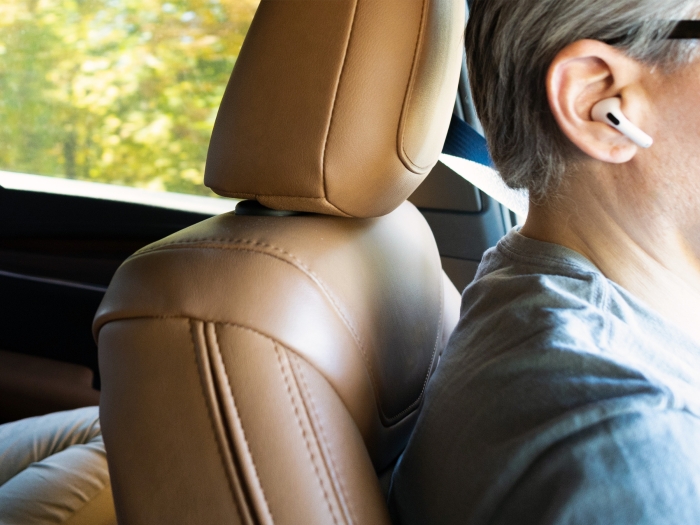 close up of airpod in ear while old man with glasses drives and light brown leather seats in car