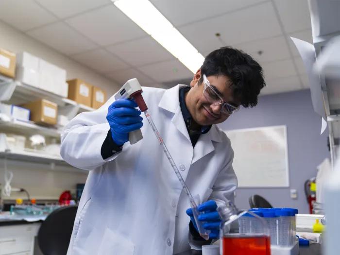 young researcher smiling in a lab holding a pipette