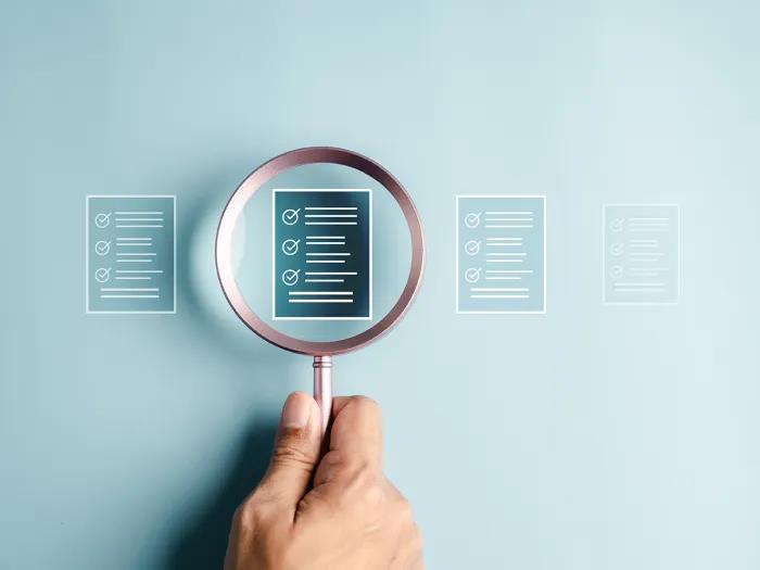 Photo of a hand holding a magnifying glass over a checklist.