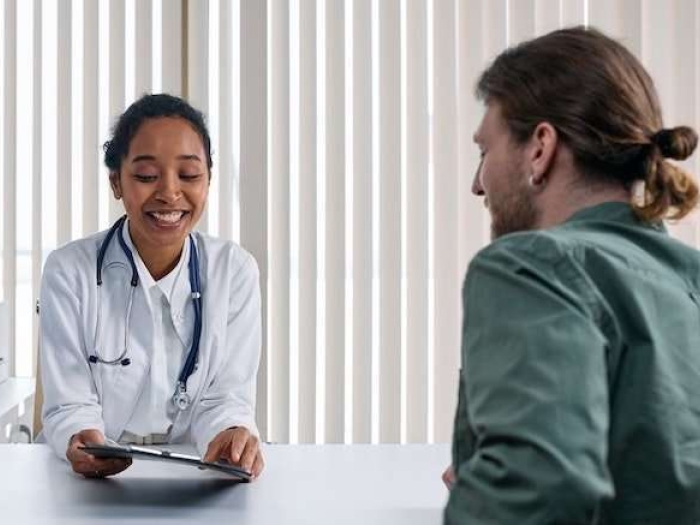 Young medical professional smiles & shows young man with man bun information on clipboard