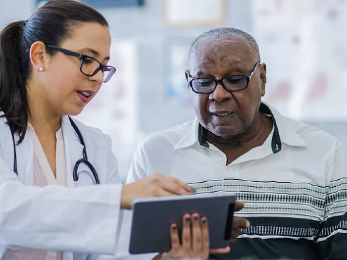 Female Medical Professional shows older gentleman information on a tablet
