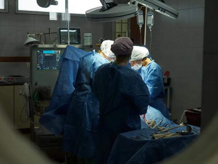 looking at surgeons operating in room with scrubs and scrub hats on through a door window