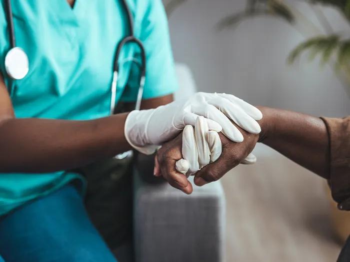 Clinician wearing medical gloves holds a patient's hand