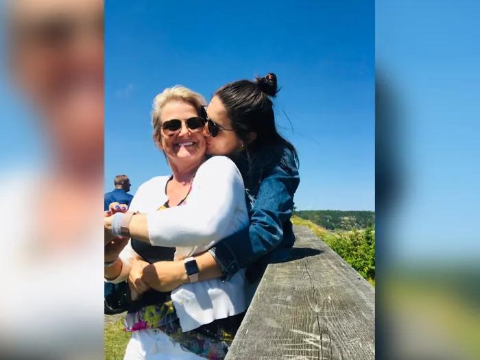 older daughter hugging and kissing her mom outside with blue sky by a rock