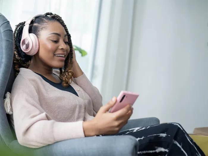 woman sitting and smiling while listening to a podcast on headphones