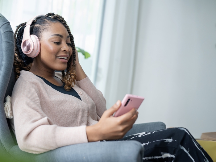 woman sitting and smiling while listening to a podcast on headphones