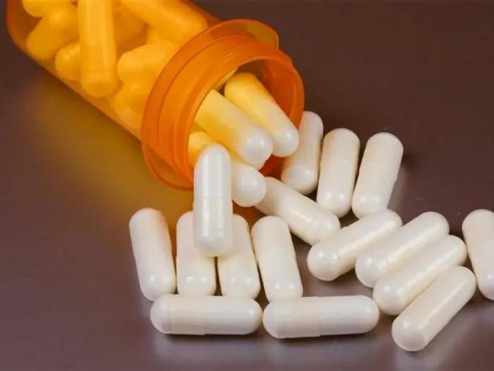 white pills falling out of orange pill bottle on a brown surface