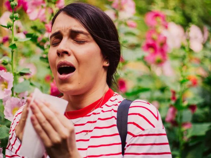sneezing woman with flowers in background red shirt