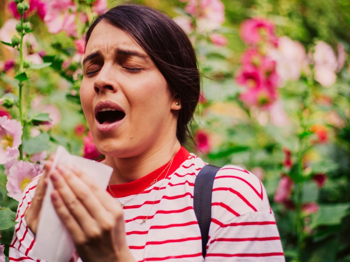 sneezing woman with flowers in background red shirt
