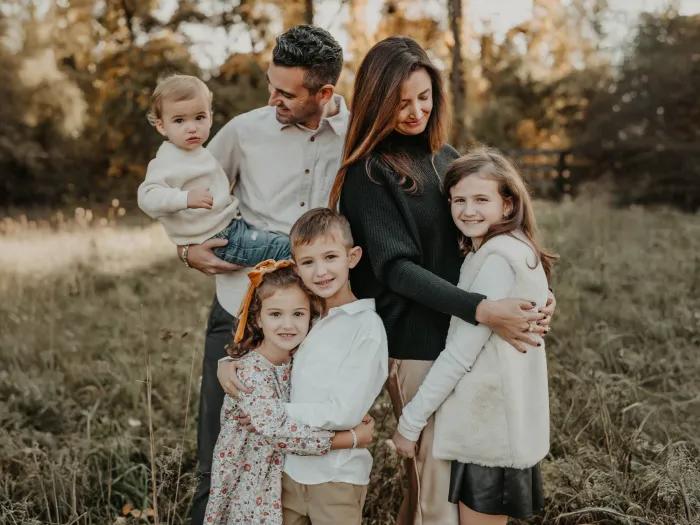 family photo mom dad and four kids in soft white beige and black clothes outside in field with trees behind