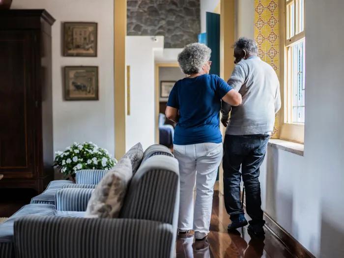older woman walking with older man look from behind in their home