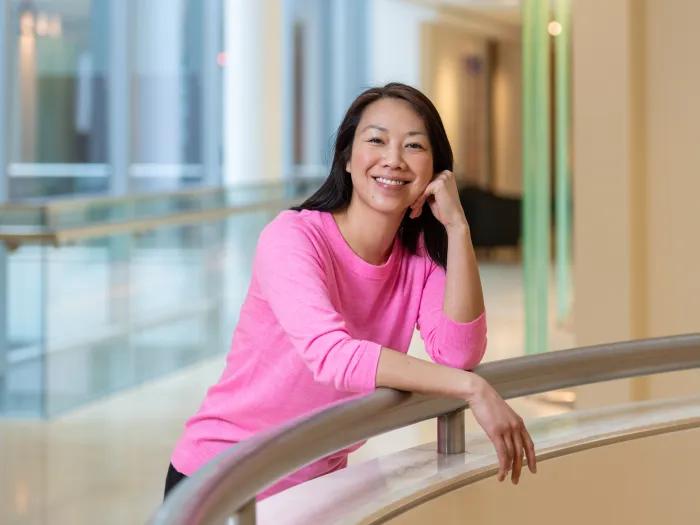 Smiling female doctor leaning on railing in a pink shirt