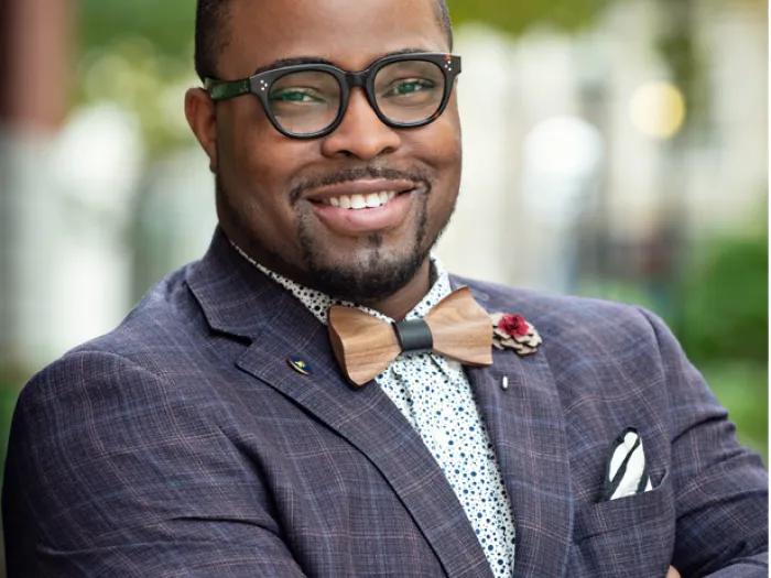 Black man wearing glasses, a dark blue suit coat and bow tie