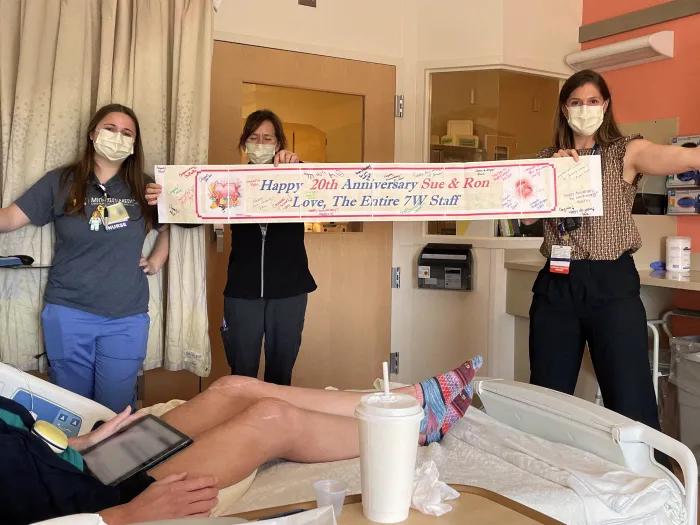 3 staff members holding up happy 20th wedding anniversary sign to patient in bed