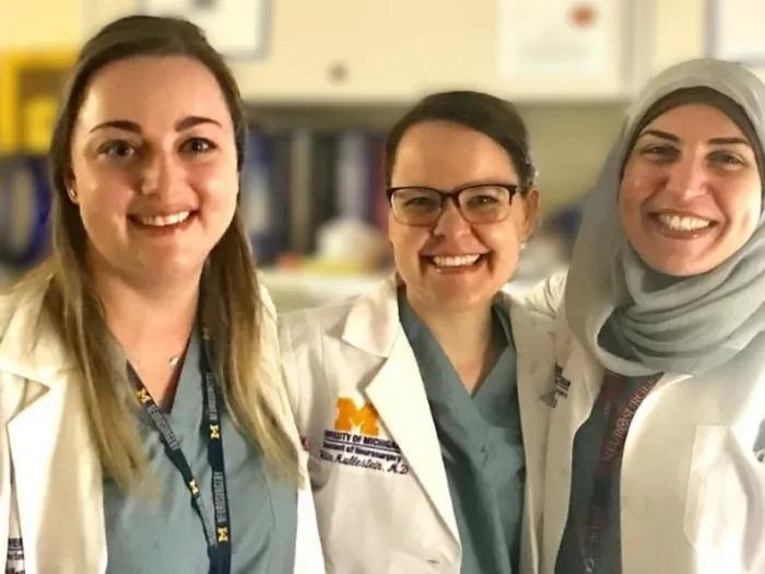 Three women doctors in white lab coats smiling 